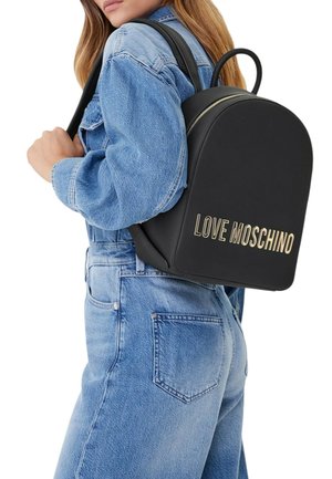 Donna con giacca di jeans blu e jeans che porta uno zaino nero Love Moschino sulla spalla.