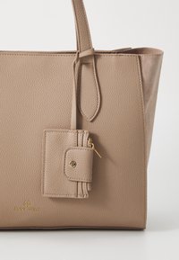 Lichtbeige textuur tote bag met twee handvatten en een afneembare ritstas. Voorzien van gouden hardware en een gegraveerd logo aan de onderkant.