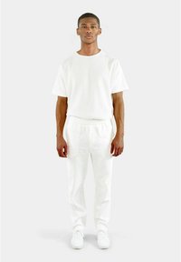 Weißes Kurzarmhemd und leichte Hose aus strukturiertem Stoff. Kombiniert mit weißen Sneakern. Einfacher, entspannter Schnitt und monochromatisches Design.