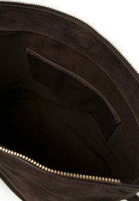 Interno di borsa tote in pelle scamosciata marrone con una texture liscia, dotata di una piccola tasca e una cerniera dorata lungo il bordo superiore.