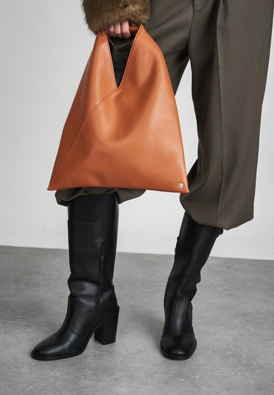 Orange syntetiskt läderväska med triangulär form och ett urgröpning handtag, parat med knähöga svarta läderstövlar med klack.