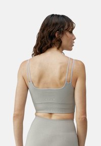Grijze aansluitende sportbeha met verstelbare banden, naadloos ontwerp en textuuraccenten. Heeft een cropped lengte en subtiele branding op de achterkant.