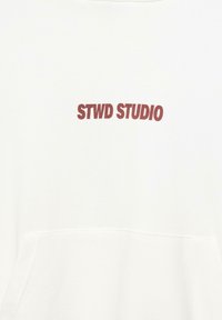 Hvid sweatshirt med en blokbogstaveret rød "STWD STUDIO" logo på forsiden, lavet af blødt bomuldsstof.