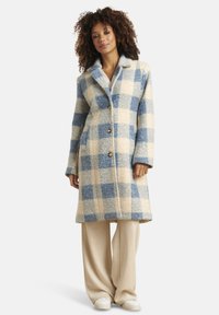 Wollmantel mit großem blau-creamfarbigen Karomuster, langen Ärmeln, spitzem Kragen und vorne mit Knöpfen zu schließen. Mit Seitentaschen.