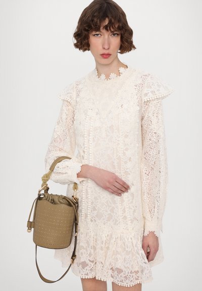 Spitzenkleid in Off-White mit floralen Mustern, Rüschenärmel und einem gewellten Ausschnitt, kombiniert mit einer beigefarbenen Bucket Bag mit perforierten Details.
