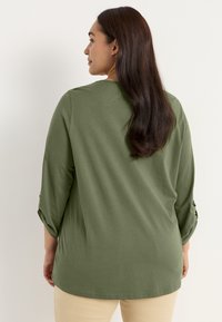 Olivgrünes Langarmshirt mit lockerer Passform, mit hochgerollten Ärmeln und rundem Halsausschnitt, aus weichem, strukturiertem Stoff.