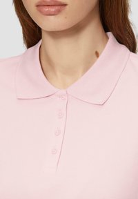 Roze polo shirt met een klassieke kraag, voorzien van een sluiting met vijf knopen en een gestructureerde stof. Subtiele stikseldetails nabij de kraag.