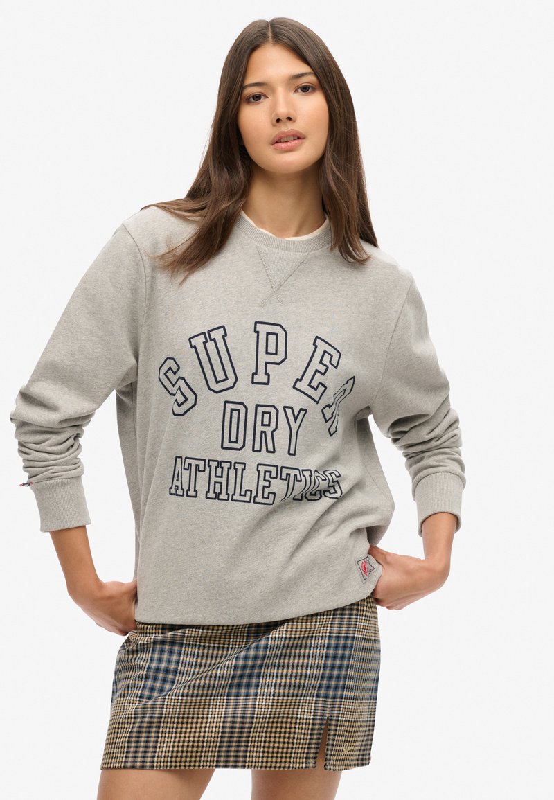 Grijze sweatshirt met de opdruk "SUPER DRY ATHLETES", gecombineerd met een geruit minirok. De sweatshirt heeft ribgebreide boorden en een halslijn.