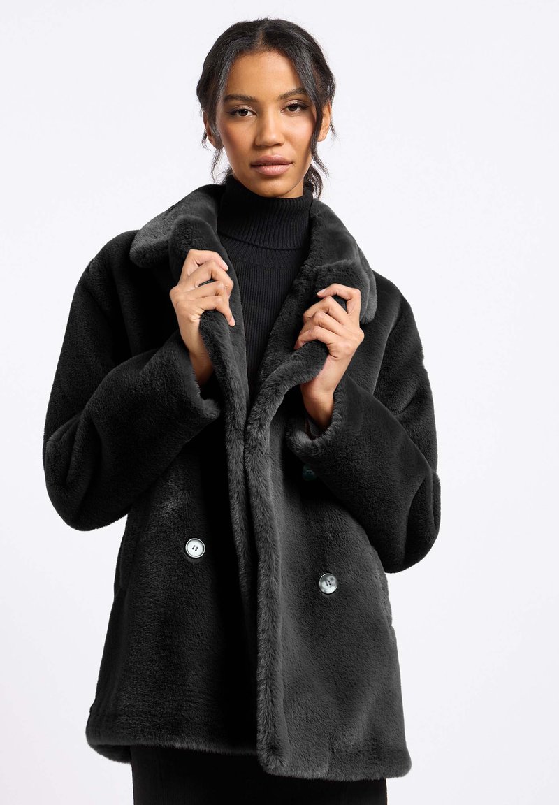 Zwarte faux fur jas met een brede kraag, dubbele knoopsluiting en lange mouwen. Zachte textuur met contrasterende blauwe knopen.