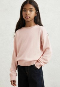 Helles rosa, gestricktes Sweatshirt mit gerippten Bündchen und Taillenbund; runder Halsausschnitt mit strukturiertem Muster verziert; getragen mit dunklen Jeans.