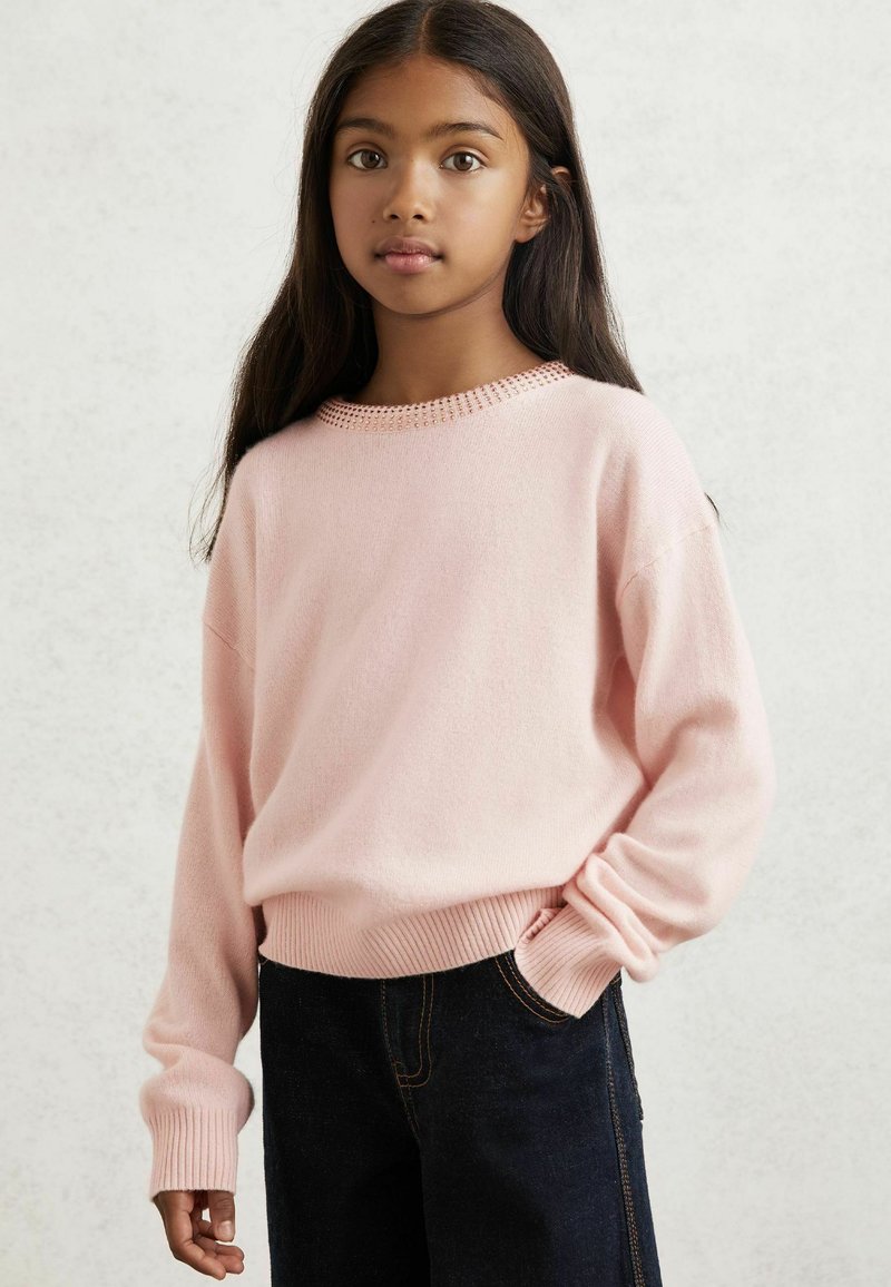 Helles rosa, gestricktes Sweatshirt mit gerippten Bündchen und Taillenbund; runder Halsausschnitt mit strukturiertem Muster verziert; getragen mit dunklen Jeans.