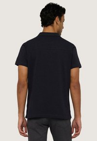 Černé bavlněné polo tričko s krátkými rukávy, límcem a čistým designem zadní části, s jemnou texturou a bez viditelných log či grafik.