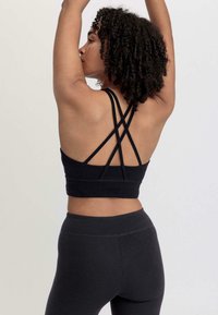Black athletic crop top with multiple crisscross straps at the back, made from a smooth, stretchy fabric, paired with dark leggings.