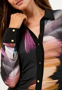 Bluză neagră cu nasturi, cu un design floral în nuanțe de roz, mov și portocaliu; nasturi aurii pe manșetele negre; textură de țesătură netedă.
