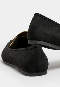 Musta mokkanahkainen tasapohjakenkä, jossa on matala korko, pyöreä kärki ja sivusomiste. Pohjat ovat sileät ja tasaiset, suunniteltu mukavaan käyttöön.