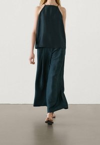 Haut sans manches en bleu sarcelle, fabriqué en tissu léger, associé à un pantalon à jambes larges. La tenue a une coupe décontractée et un design minimaliste.