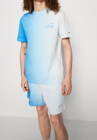 Souprava z lehkého modrého gradientního trička a šortek. Bavlněný materiál, krátké rukávy, logo na hrudi, jemná textura a volný střih.