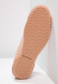 Reebok sneakersula, ljus persikofärg med en texturerad gummiyta. Har ett mönstrat mönster och varumärke på hälen.