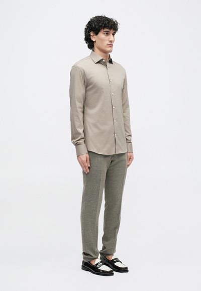 Light beige long-sleeve shirt with button placket, paired with textured gray trousers and black loafers with white accents. Flat background.