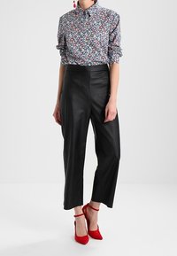 Chemise à motifs floraux avec manches retroussées, associée à un pantalon en cuir noir cropped et des chaussures à talons rouges avec des brides de cheville.
