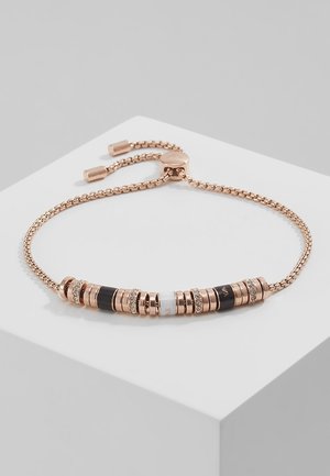 Bracelet à chaîne ajustable en or rose avec des anneaux noirs et incrustés de diamants disposés symétriquement sur un bloc d'exposition blanc.