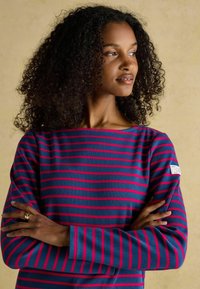 Pikkade varrukatega triibuline pluus, kus on tumedate siniste ja roosa triibud, ümar kaelus ning logo silt vasakul varrukal. Pehme, tekstureeritud kangas.