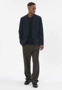 Tengerészkék blézer, két gombbal, fekete pólóval és barna nadrággal párosítva. Fekete cipők egészítik ki az öltözetet. Simább anyagtextúra.