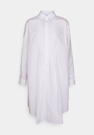 Cămașă albă cu mânecă lungă și închidere cu butoane, având pliseuri și embellishments răsfirate pe față. Material neted, croială lejeră.