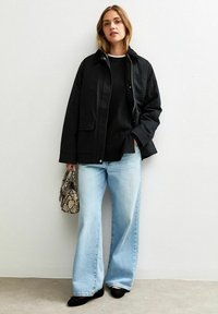 Czarna kurtka na zamek, połączona z czarnym swetrem, jasnoniebieskimi spodniami typu wide-leg oraz torebką ze skóry wężowej. Czarne płaskie buty.