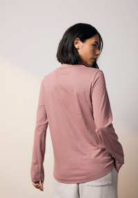 Långärmad, rosa skjorta gjord av mjukt tyg, med rund halsringning och avslappnad passform, kombinerad med ljusgrå byxor.