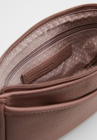 Hnědá syntetická peněženka uvnitř s přihrádkou na zip a podšívkou s puntíky a koženou etiketou. Hladký povrch a strukturovaný tvar.