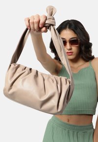 Beige læderhåndtaske med samlingsdesign og knyttet stofrem, der har en glat tekstur og minimalistisk stil.