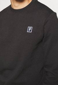 Schwarzer Sweatshirt mit rundem Ausschnitt, aus weichem Stoff; verfügt über ein kleines, weiß-blaues gesticktes Logo auf der Brust.