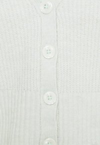 Ljusgrön stickad cardigan med ett texturerat mönster, v-ringning och sex stora runda knappar framtill. Mjuk, ribbad tyg.