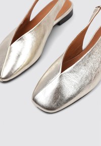 Zapatos slingback plateados metálicos con diseño de punta, que presentan una textura suave y un tacón bajo cuadrado.