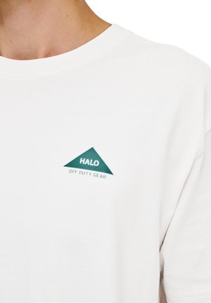 Biała bawełniana koszulka z zielonym trójkątnym logo, z napisem "HALO OFF DUTY GEAR" umieszczonym pod nim na piersi. Prosty design.