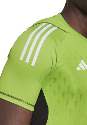 Groene sportieve shirt met zwarte accenten, voorzien van een witte driedubbele streepontwerp op de schouders en een gestructureerd patroon op de stof.