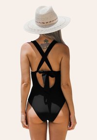 Bañador negro de una pieza con tirantes cruzados, corte en la espalda y detalle de lazo. Textura suave, diseño minimalista, adecuado para nadar o usar en la playa.