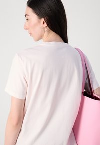 Maglietta in cotone rosa chiaro con maniche corte, vista da dietro, abbinata a una grande borsa tote strutturata rosa con interno rosso.