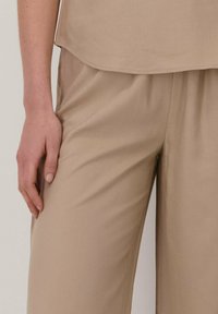 Beige linnenmix top met een afgeronde zoom, gecombineerd met bijpassende wijde broek. Gladde textuur, ontspannen pasvorm, geen zichtbare patronen of hardware.