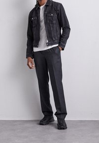 Svart denimjacka med två bröstfickor, grå t-shirt och mörkgrå byxor. Klumpiga svarta sneakers kompletterar outfiten.