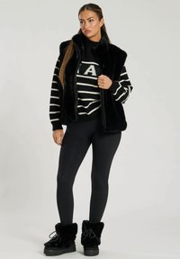 Svart konstläder väst över en randig svart och vit tröja, i kombination med svarta leggings och svarta ankelboots med foder av päls. Enkelt design.