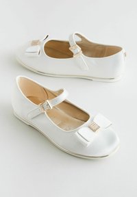 Scarpe da ballo bianche con punta arrotondata, un fiocco sulla parte anteriore e piccoli dettagli dorati. Presentano una cinghia con fibbia e una superficie liscia.