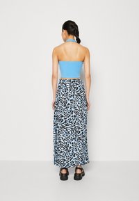 Crop top à bretelles bleu clair associé à une longue jupe ornée d'un imprimé animalier noir et bleu. Des sandales noires à plateforme complètent le look.
