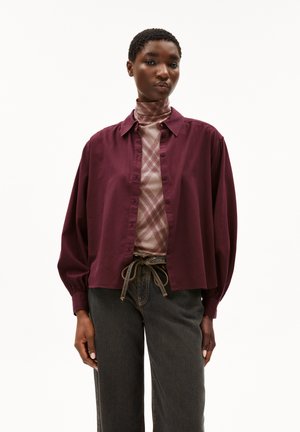 Burgunderfarbene Hemdbluse mit einem lockeren Schnitt, Ballonärmeln und einem Kragen, über einem gemusterten Rollkragenpullover getragen und kombiniert mit dunklen Jeans.