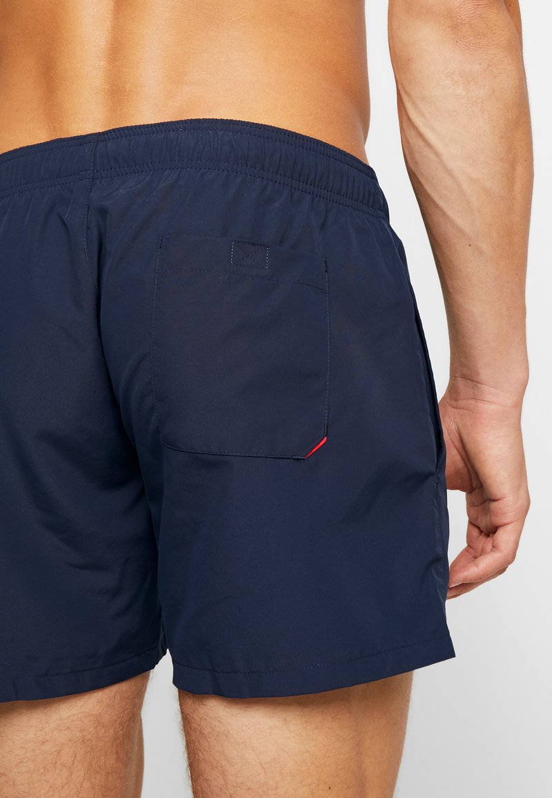 Marineblaue Badeshorts mit elastischem Bund, einer einzigen Gesäßtasche und einem kleinen roten Akzent an der Taschennaht. Glattes, leichtes Material.