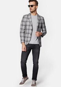 Szary kratkowany żakiet z dwoma guzikami, w zestawieniu z szarym t-shirtem, ciemnymi dżinsami i szarymi trampkami. Okulary przeciwsłoneczne dopełniają stylizację.