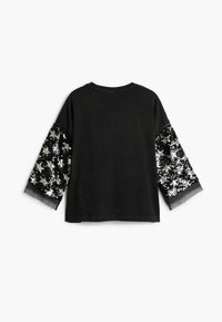 Schwarzes Hemd mit weiten Ärmeln aus silbernem und schwarzem Paillettenstoff. Der Rücken hat einen einfachen Rundhalsausschnitt und eine legere Passform.