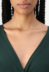 Robe verte à col en V en tissu lisse, présentant une silhouette ajustée et un design minimaliste. Le teint de la peau est visible sans motifs.