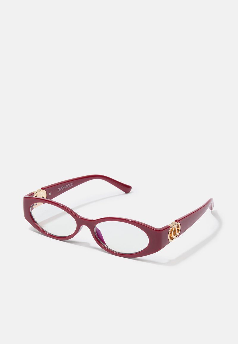 Červené plastové brýle ve tvaru oválu s průhlednými čočkami. Obsahují zlaté kovové detaily na spáncích a mají elegantní moderní design.